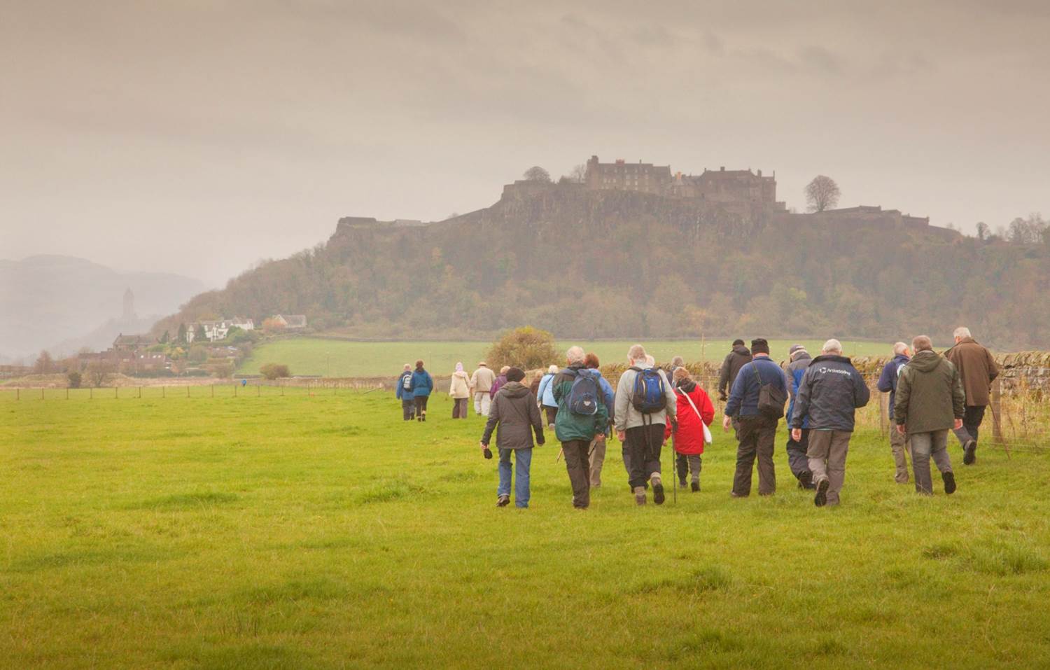 A group of walkers on a field with a hill and castle in the distance