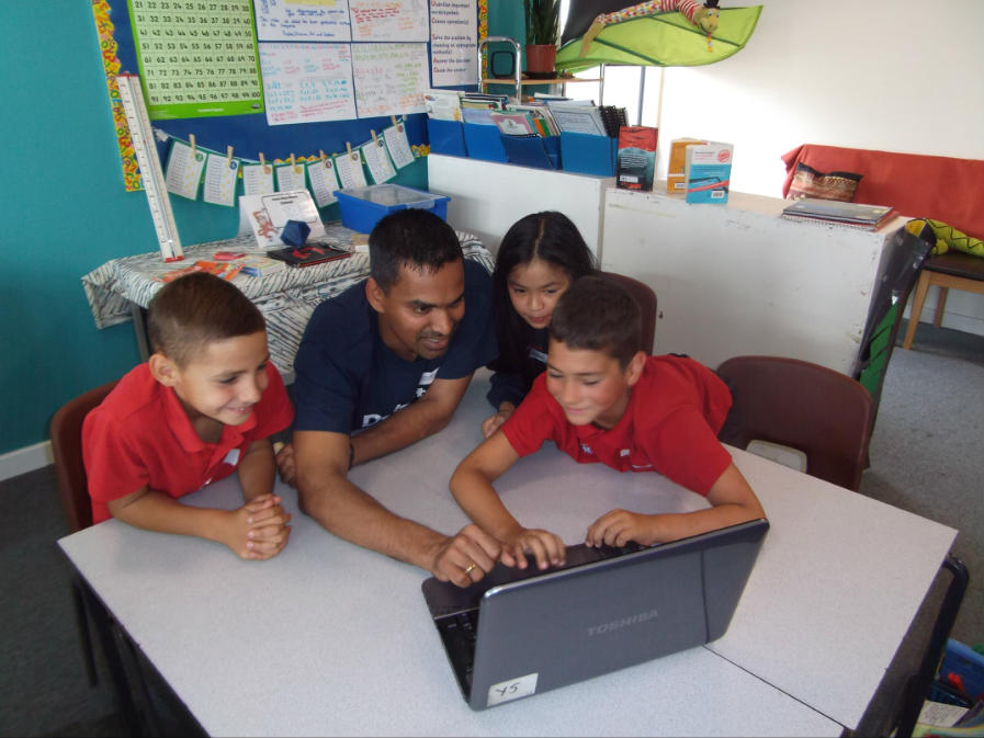 Three young people and one adult in a classroom looking at a laptop