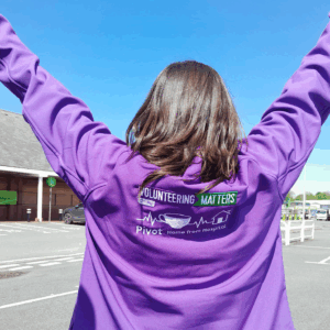 A person with their arms in the air. The photograph is on their back as they are wearing a jumper with the Volunteering Matters logo