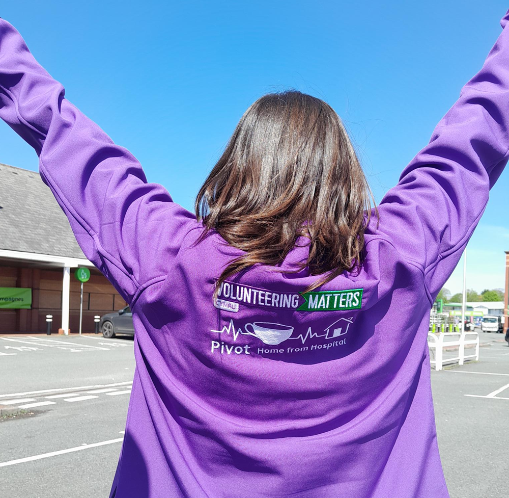 A person with their arms in the air. The photograph is on their back as they are wearing a jumper with the Volunteering Matters logo