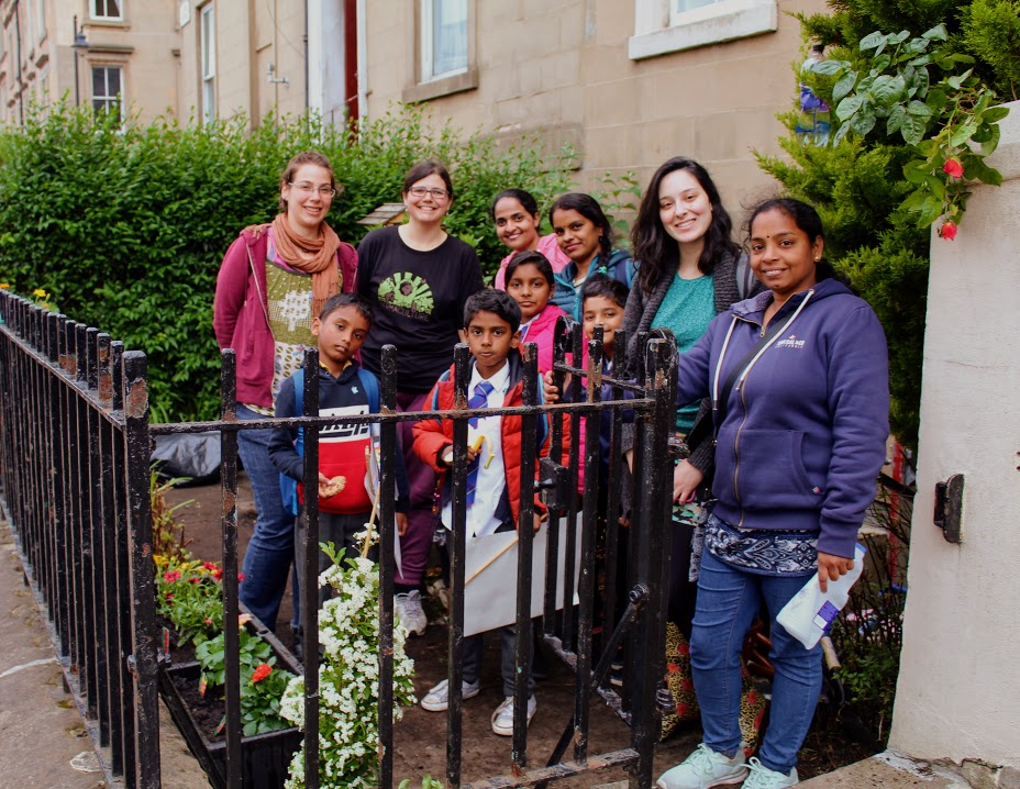 10 people stood outside a building behind a fence tending to flowers