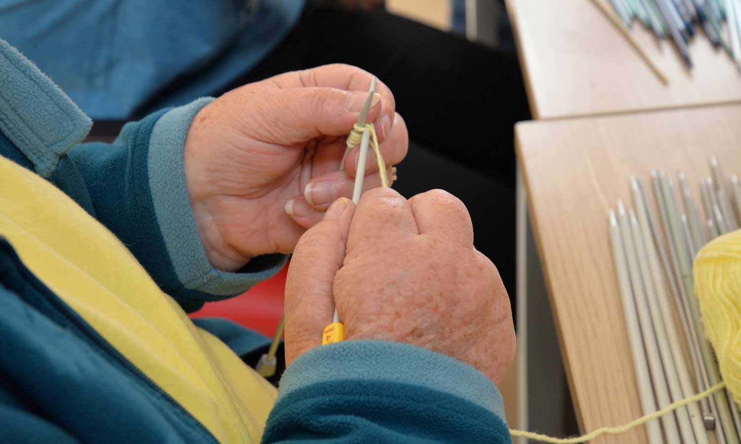 Hands of someone knitting with thread and two knitting sticks