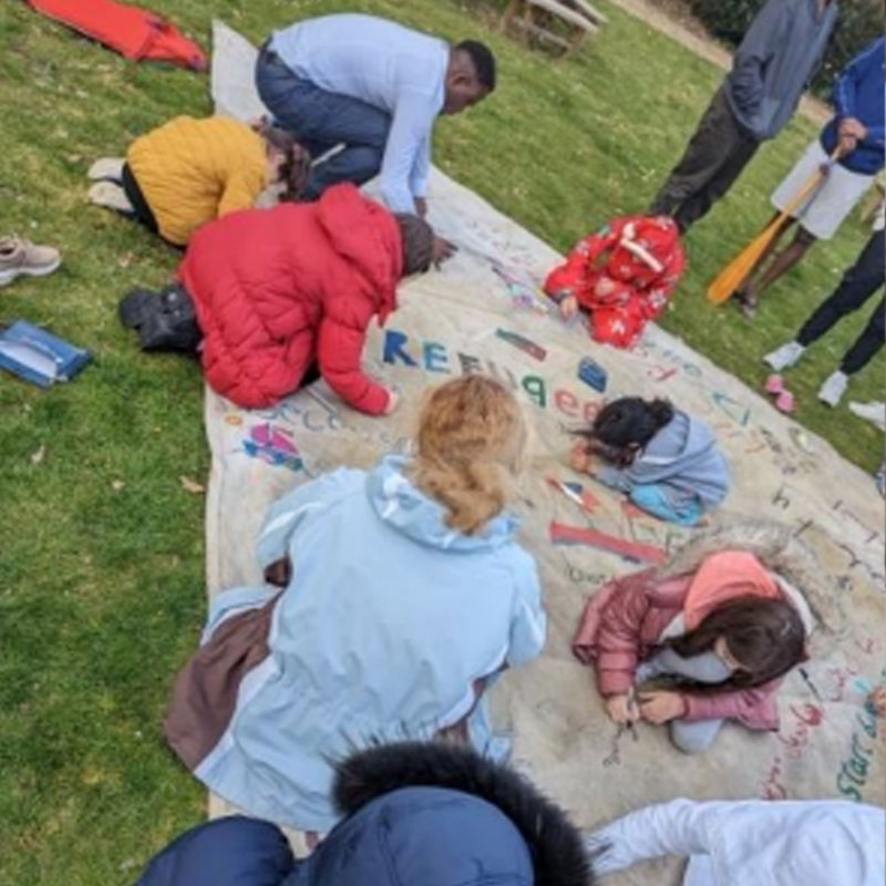 A group of people working on a fabric banner on the floor in a field