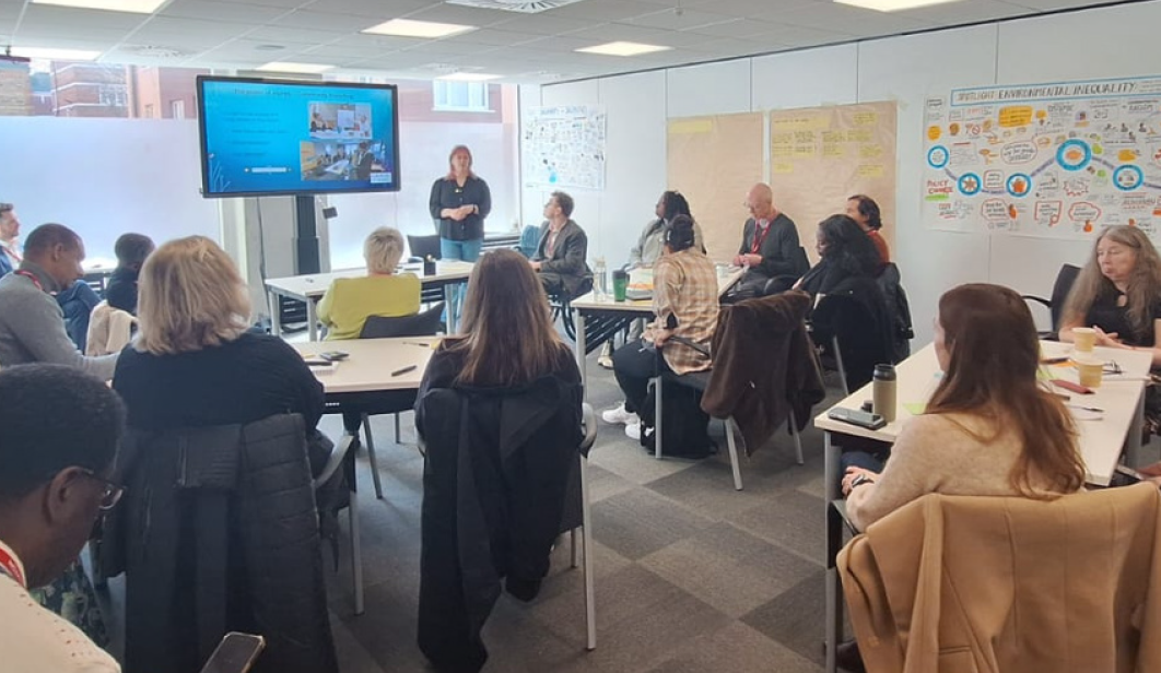 A group of people in a room looking at a person standing up next to a screen