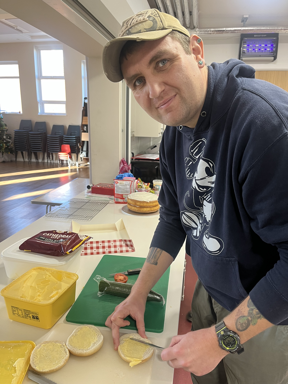 A person in a kitchen space looking at the camera buttering a piece of bread
