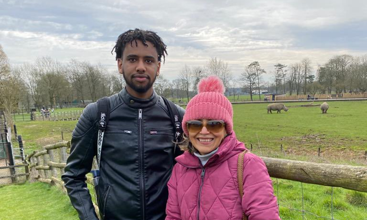 Two people stood in front of a fence in a field. Both are wrapped up in a thick jacket