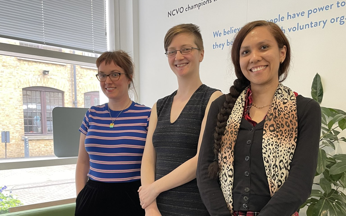 Three people posing for the camera in an office with the words NCVO behind them