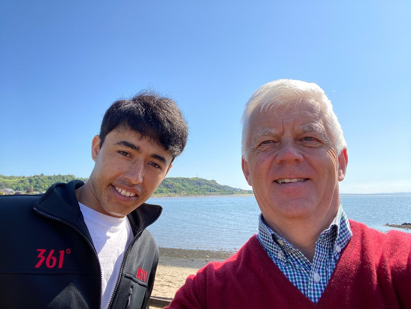 Two people standing side by side taking a selfie by the beach