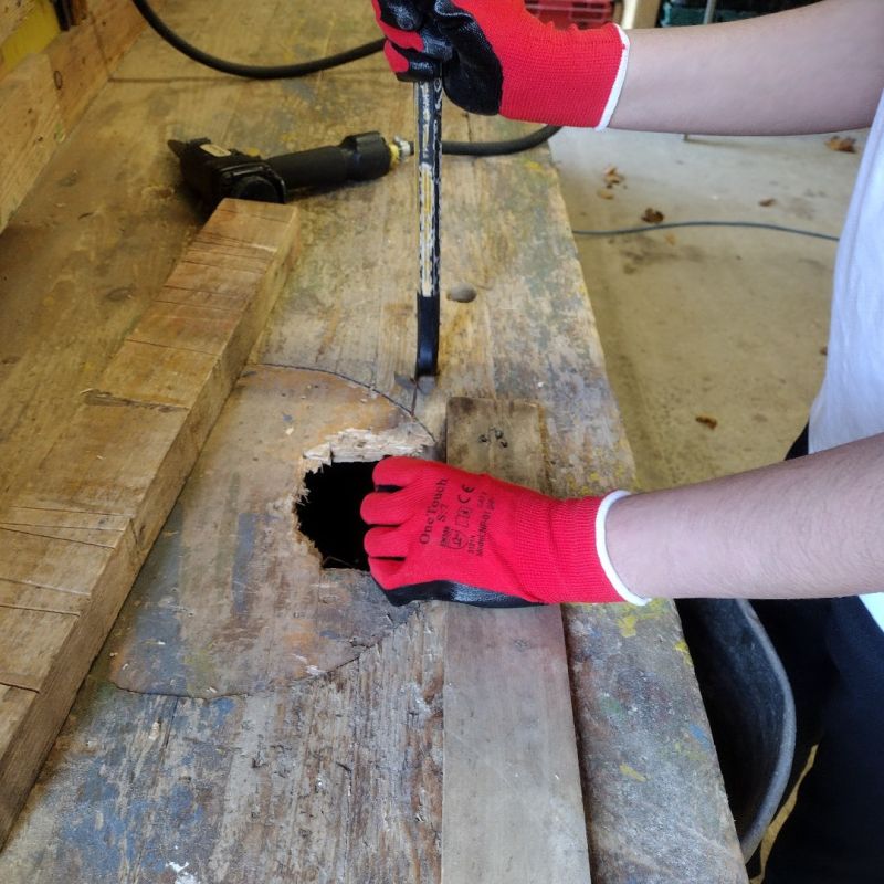 A person with red safety gloves using a chisel on wood