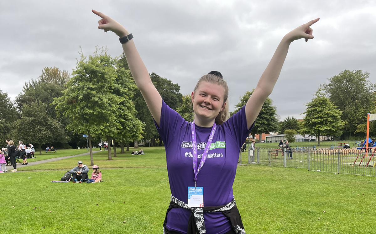 Person raising their arms in the air wearing a purple tshirts and a medal around their neck