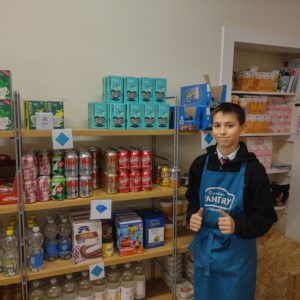 A young person standing in a pantry in front of cans of food on four shelves