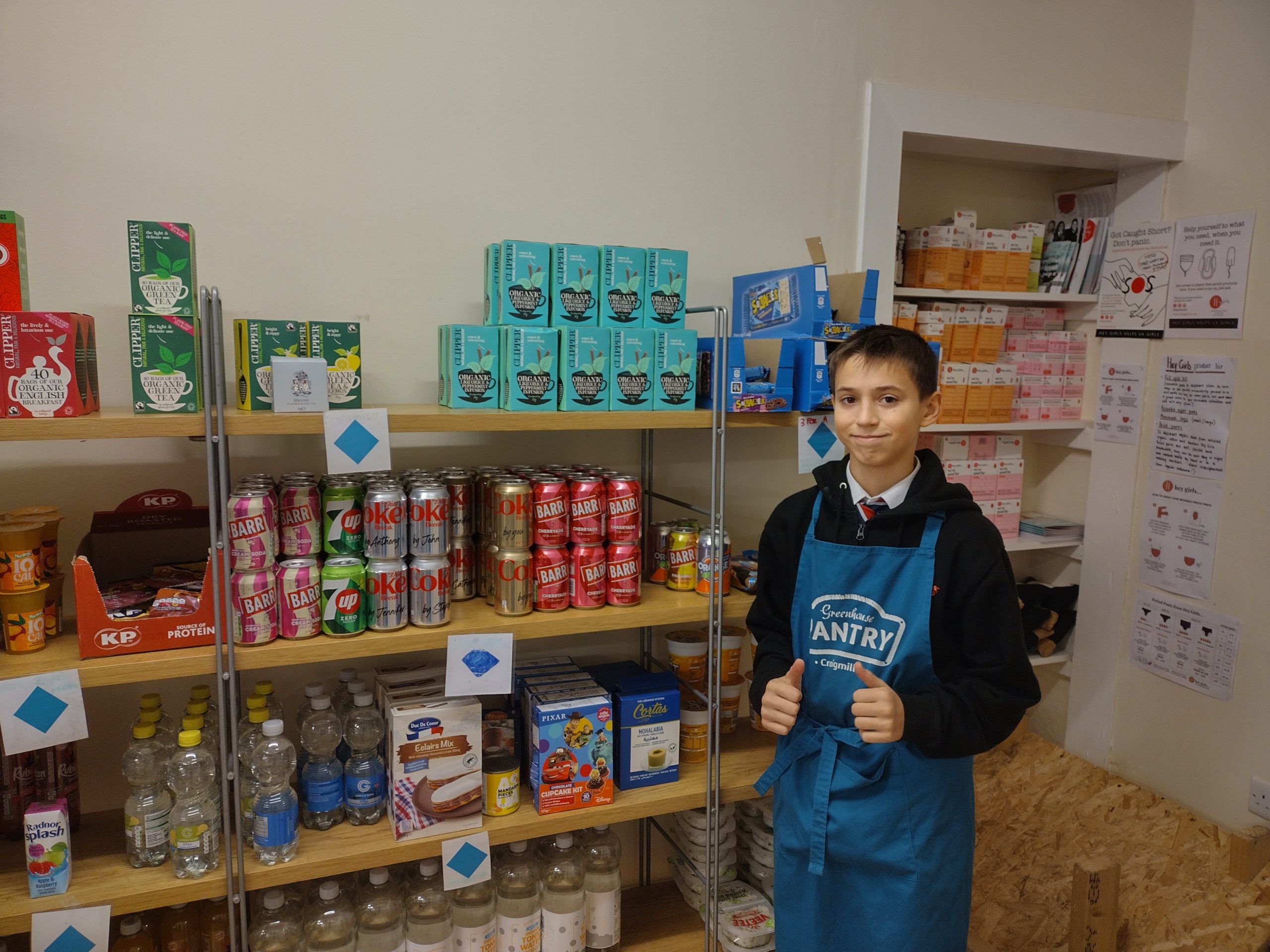 A young person standing in a pantry in front of cans of food on four shelves