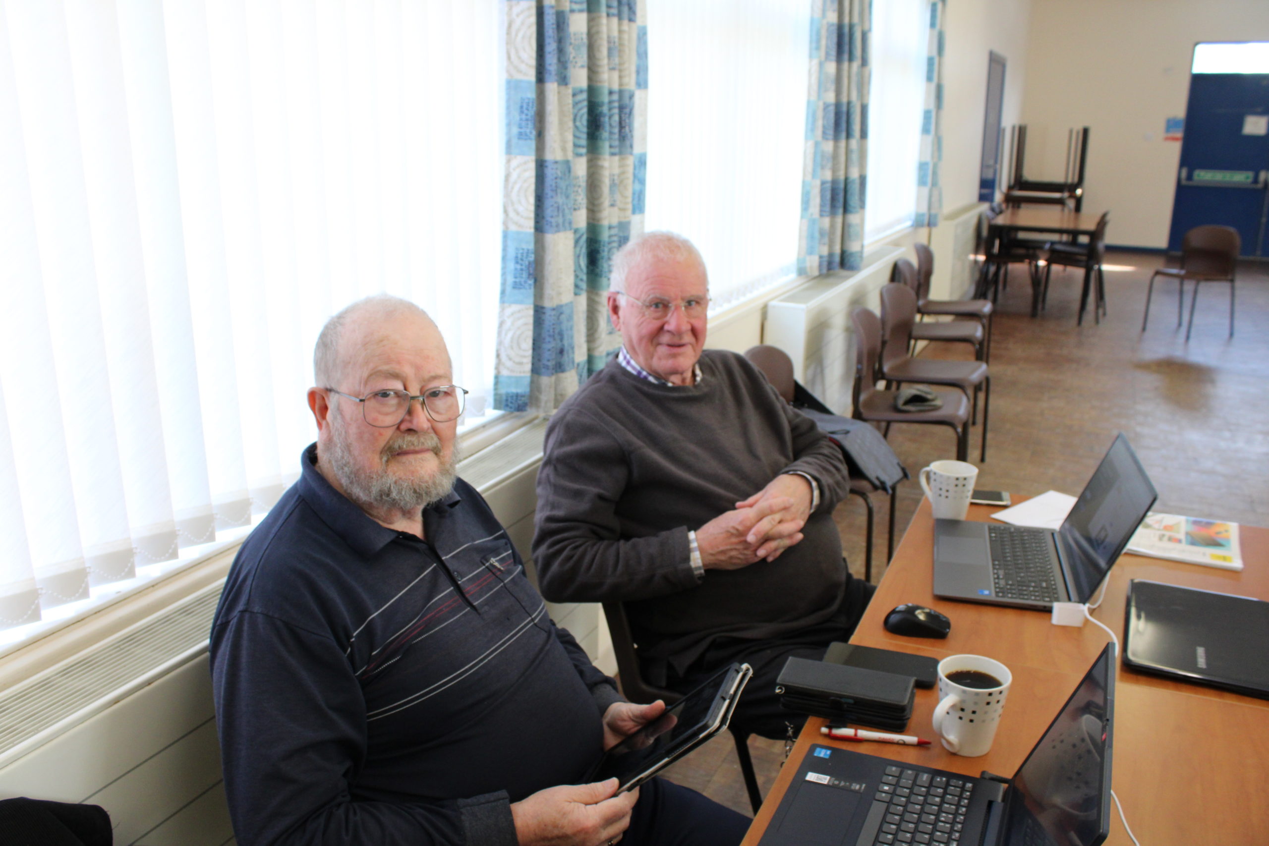 Image of two men sat down inside a village hall