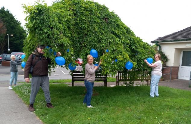 A group of people outside standing separately with blue balloons