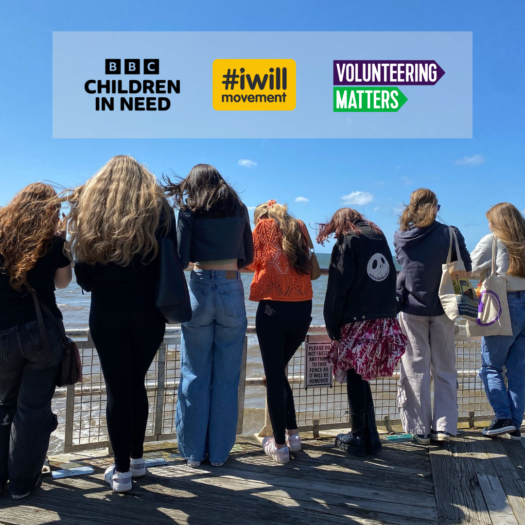 Seven young people looking over to the sea in Blackpool leaning on a metal railing