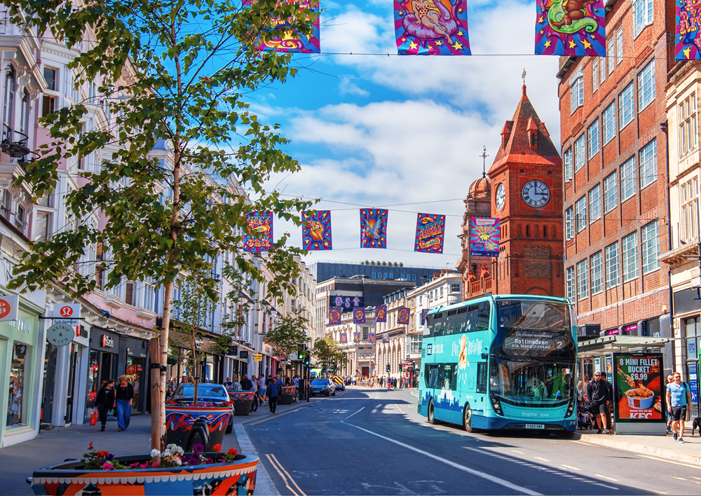 A photo of a high street in Brighton featuring a blue bus, banners draped across the street and numerous shops