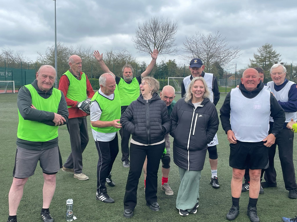 Chair and CEO of Volunteering Matters stood outside on a football pitch surrounded by players