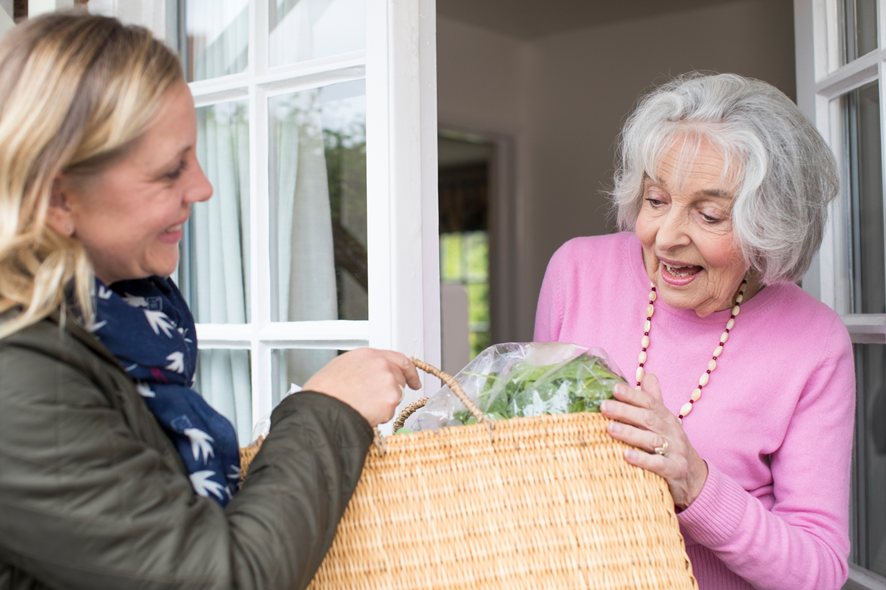 A woman handing over a bag of items to an older person at their doorstep